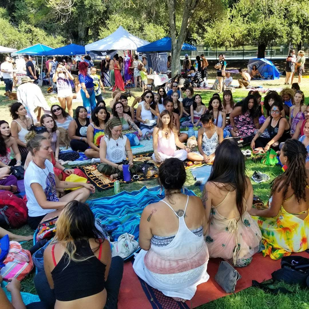 Women seated on mandala blankets in a circle, facing inward in conversation.