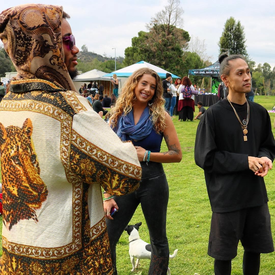 Three friends in conversation at a gathering, one in a vivid gold-patterned shirt — the 'spiritual gangsters' style.